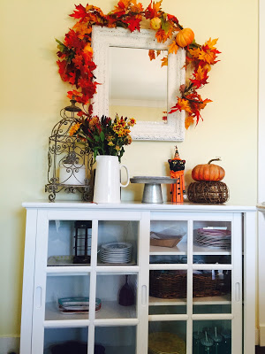 fall leaf garland wrapped around mirror over white cupboards