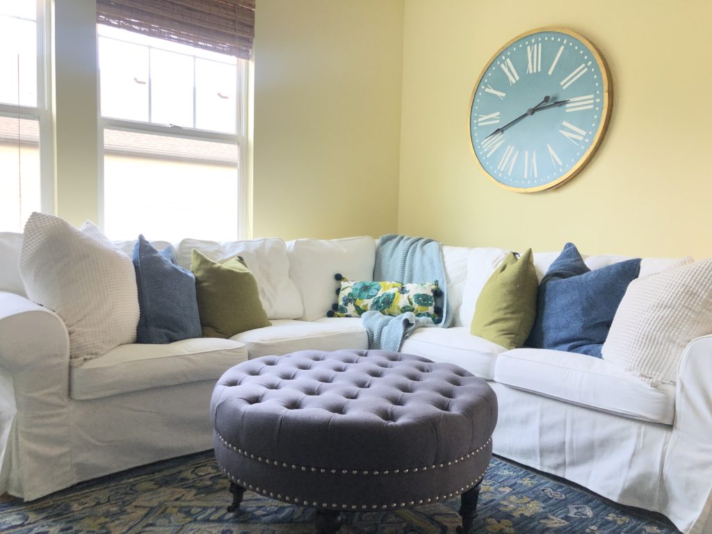 Light and airy family room. White sofa, lime green and navy pillows. Tuffted footstool. #karinskottage #lightairyroom