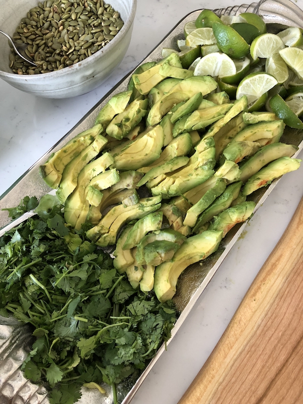 Taco salad bar platter filled with sliced avocados, cilantro and limes