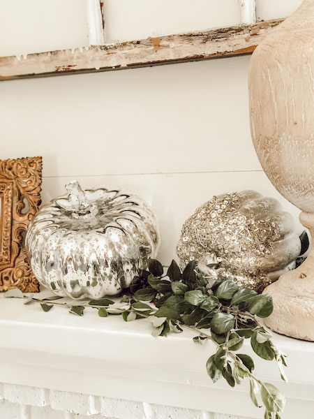 Tucking silver pumpkins on fall mantle 