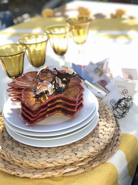 Gather supplies to create a fall outdoor tablescape easily. Using woven placemats, white dinner plates, orange leaf shaped salad plates, floral napkins and gold goblets