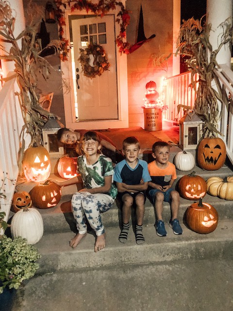 Kids on front fall porch with cornstalks and pumpkins
