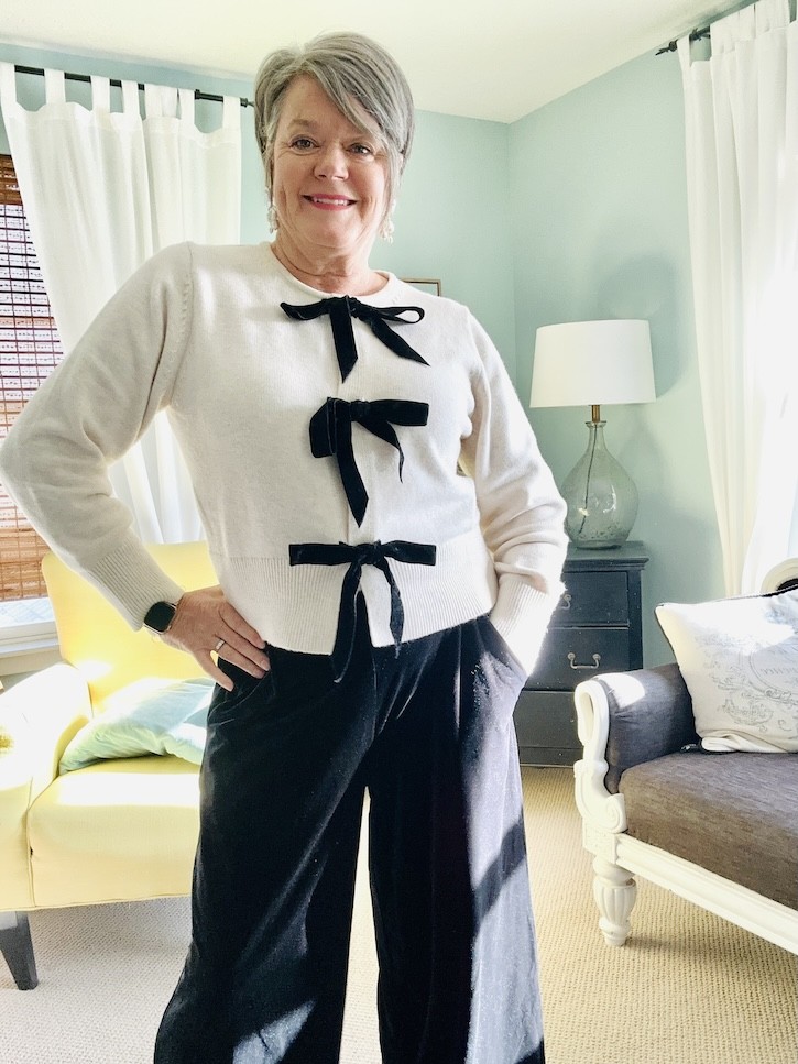 Cream bow sweater holiday outfit with velvet pants and red kitten heels.
