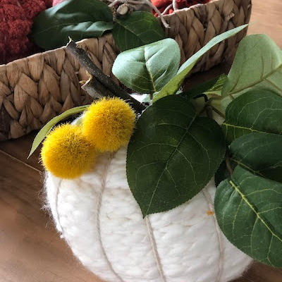 Finished creamy white yarn pumpkin with greenery and yellow floral accents