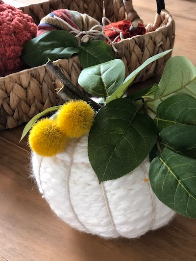 Creamy white yarn pumpkin decorated with green leaves and soft yellow pom pom flowers