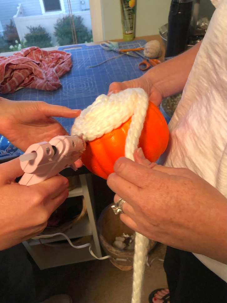 Wrapping chunky white yarn around a dollar store pumpkin with hot glue