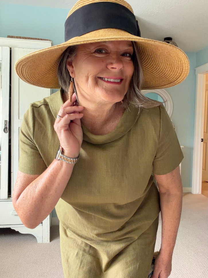 Casual summer styling of an olive green linen dress with a wide brim straw hat and woven handbag
