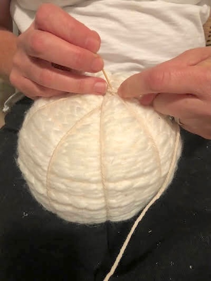 Wrapping twine around a white yarn pumpkin to create natural pumpkin sections