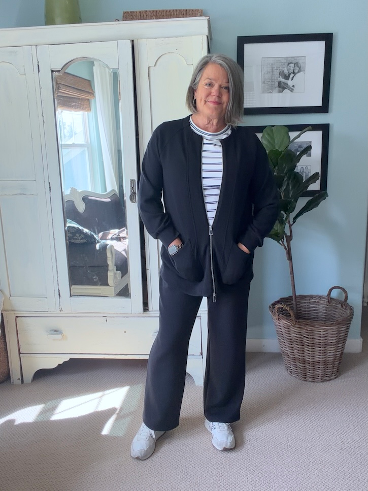 Woman over 50 wearing a comfortable black two-piece travel outfit with striped T-shirt and white sneakers.