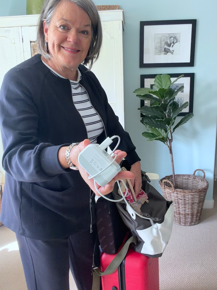 Woman holding a European travel adapter for charging a phone, Apple Watch and laptop in Italy.