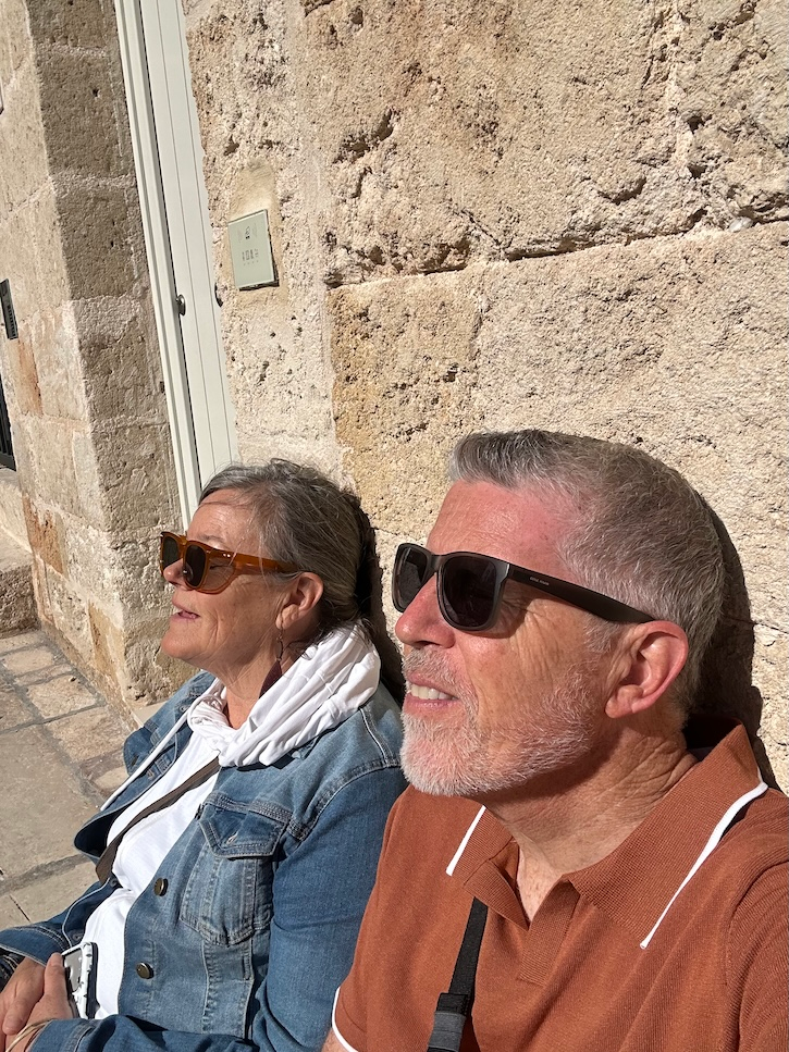 Couple sitting in the sunshine on a stone street in Italy during a day of sightseeing.