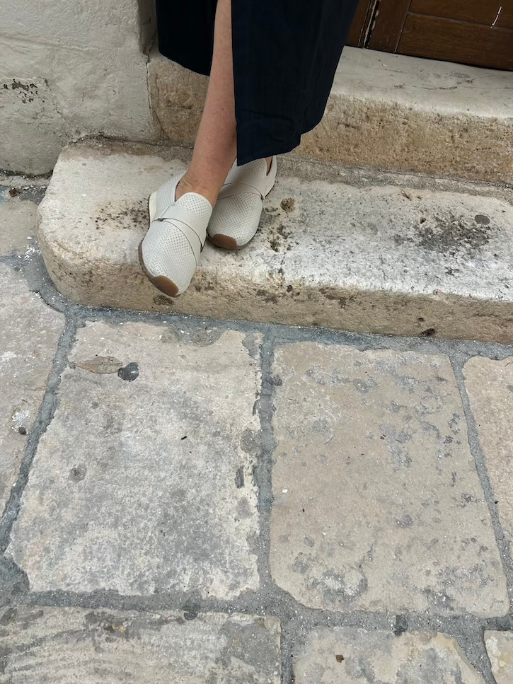 Comfortable beige BØRN knit sneakers styled with a black maxi dress for sightseeing in Italy.