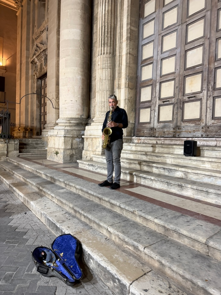 Street musician playing saxophone on the steps of a historic church in Italy at night.