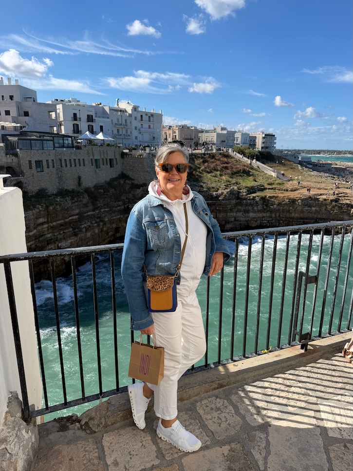Woman over 50 exploring a narrow stone street in Italy wearing a white sweatshirt and denim jacket.